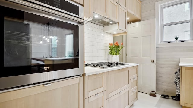 kitchen with wooden walls, backsplash, under cabinet range hood, light countertops, and stainless steel appliances