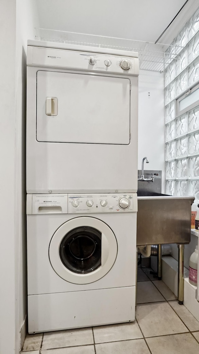 clothes washing area with light tile patterned floors, stacked washer / drying machine, and a sink