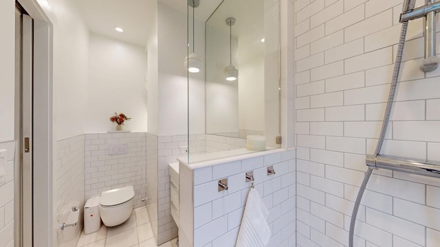 full bathroom featuring walk in shower, a wainscoted wall, toilet, tile patterned floors, and tile walls