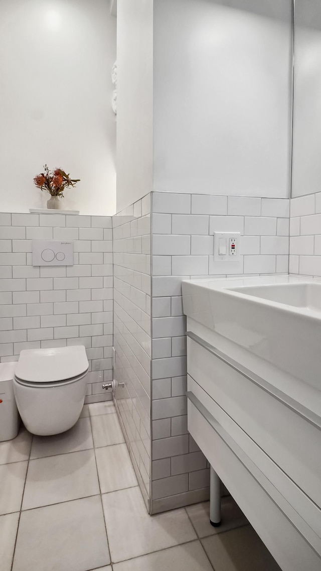 half bath with tile patterned floors, wainscoting, toilet, and tile walls