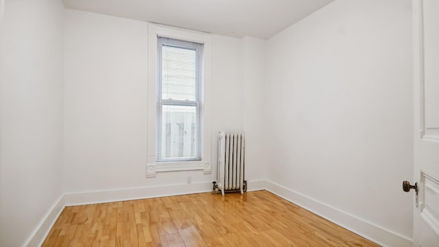 unfurnished room with baseboards, light wood-style flooring, and radiator heating unit