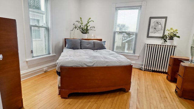 bedroom with multiple windows, radiator, and light wood finished floors