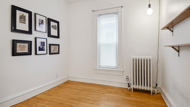 empty room featuring baseboards, radiator heating unit, and light wood finished floors