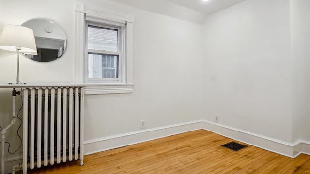 spare room with hardwood / wood-style floors, radiator, baseboards, and visible vents