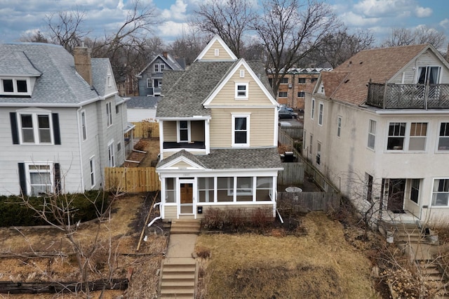 view of front of property featuring fence, a residential view, a sunroom, and a shingled roof