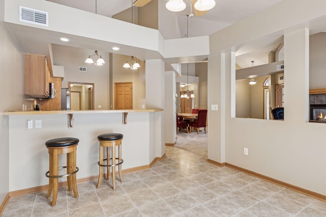 kitchen with a peninsula, a breakfast bar, visible vents, light countertops, and decorative light fixtures