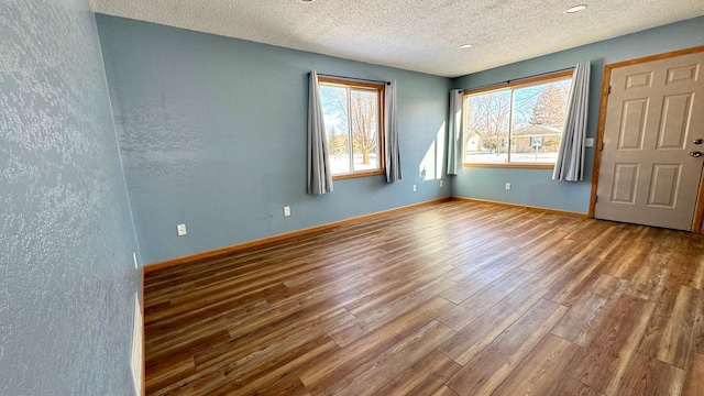 empty room with a textured wall, a textured ceiling, baseboards, and wood finished floors