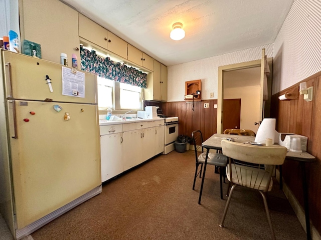 kitchen with light countertops, light carpet, wood walls, cream cabinets, and white appliances