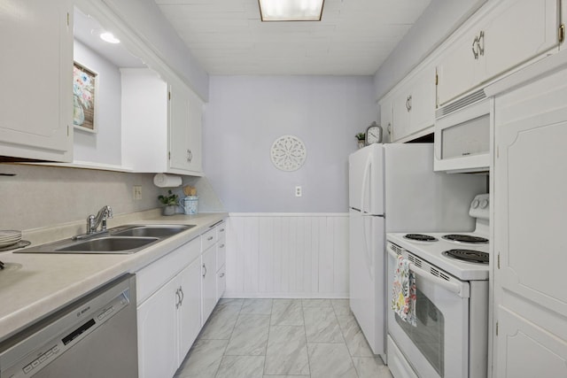 kitchen with white appliances, a wainscoted wall, marble finish floor, white cabinetry, and a sink