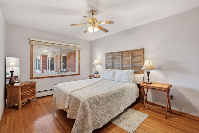 bedroom with a baseboard heating unit, a ceiling fan, baseboards, and hardwood / wood-style flooring