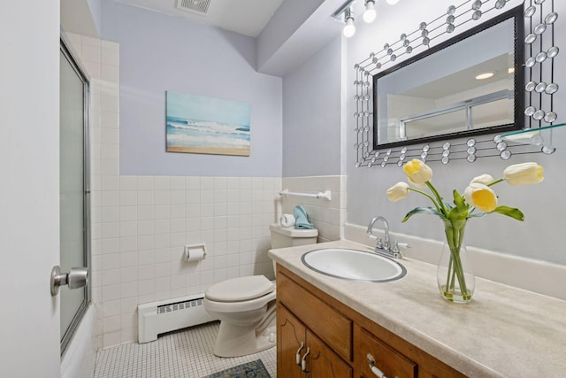 full bath with toilet, tile patterned floors, vanity, a baseboard heating unit, and tile walls