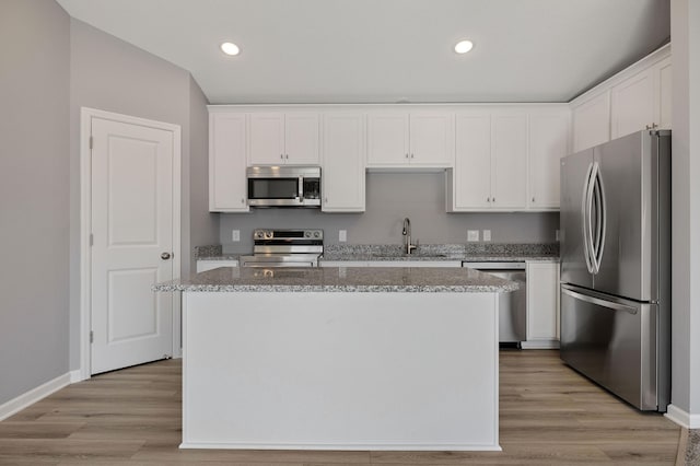 kitchen featuring sink, light stone counters, a center island, appliances with stainless steel finishes, and white cabinets