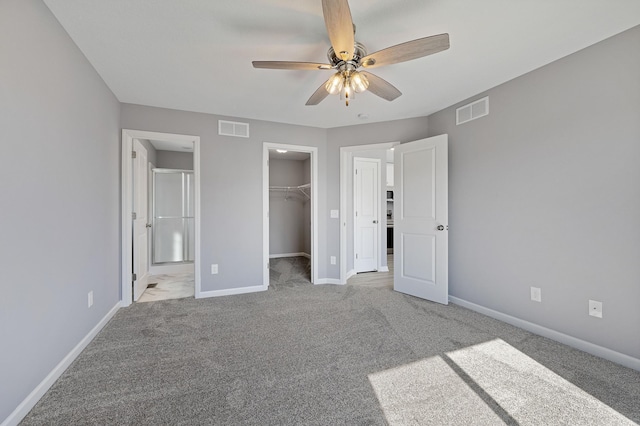 unfurnished bedroom with a spacious closet, ceiling fan, light carpet, ensuite bath, and a closet