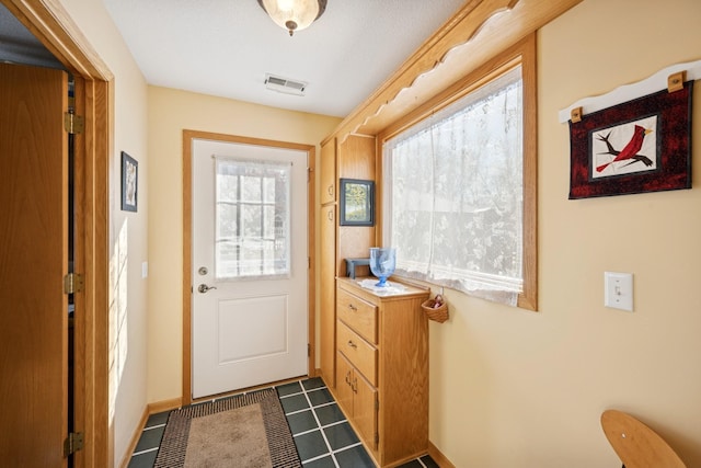 doorway with dark tile patterned flooring, visible vents, and baseboards