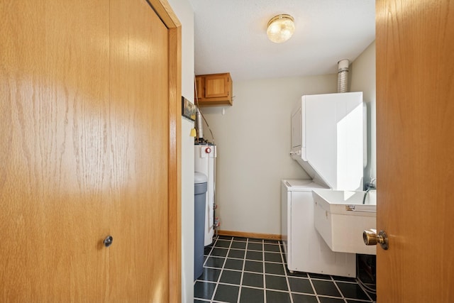 clothes washing area featuring cabinet space, baseboards, dark tile patterned flooring, stacked washer and clothes dryer, and water heater