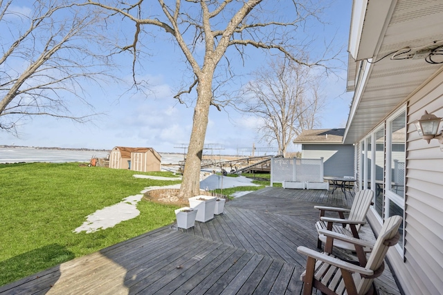 wooden terrace featuring a water view, a shed, an outbuilding, and a yard