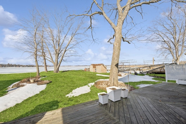 wooden terrace featuring a water view, a lawn, an outdoor structure, and a storage unit