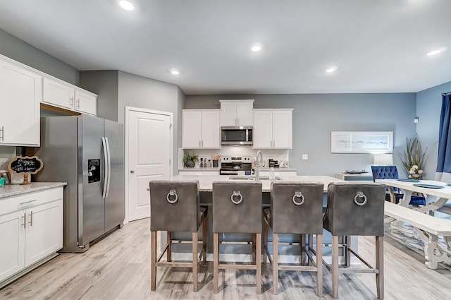 kitchen with a breakfast bar area, stainless steel appliances, light stone countertops, white cabinets, and a center island with sink