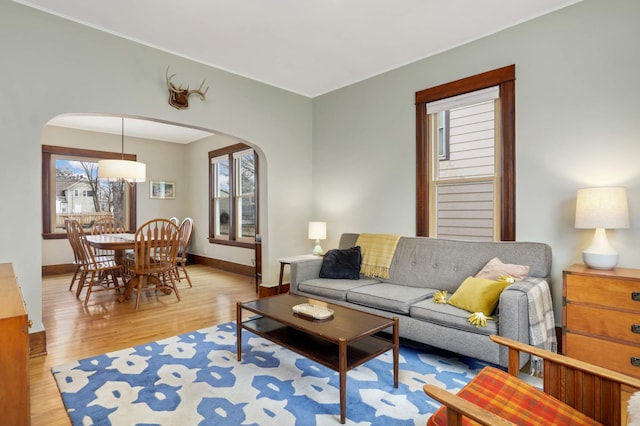 living room with arched walkways, light wood-style flooring, and baseboards