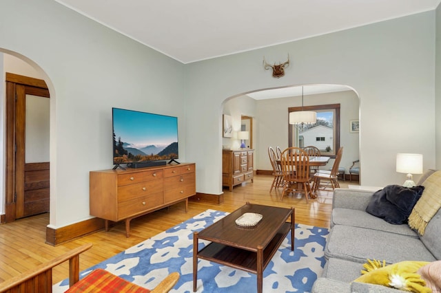 living room featuring arched walkways, baseboards, and light wood finished floors