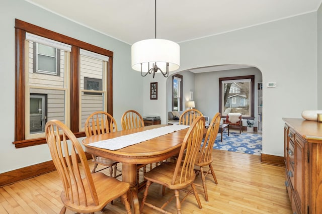 dining area featuring ornamental molding, arched walkways, light wood-style flooring, and baseboards