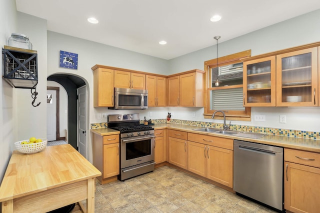 kitchen with appliances with stainless steel finishes, light countertops, glass insert cabinets, and hanging light fixtures