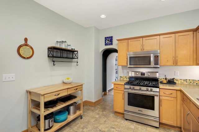 kitchen with arched walkways, light countertops, light brown cabinetry, appliances with stainless steel finishes, and baseboards