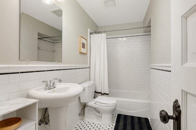 bathroom with shower / bath combo, visible vents, wainscoting, toilet, and tile walls