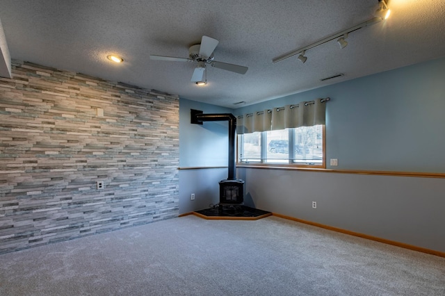 carpeted spare room with a wood stove, a textured ceiling, a ceiling fan, and baseboards