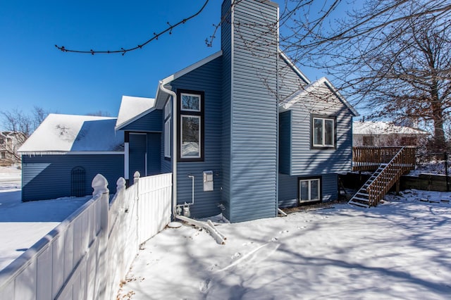 view of snow covered exterior featuring a chimney, a wooden deck, and stairway