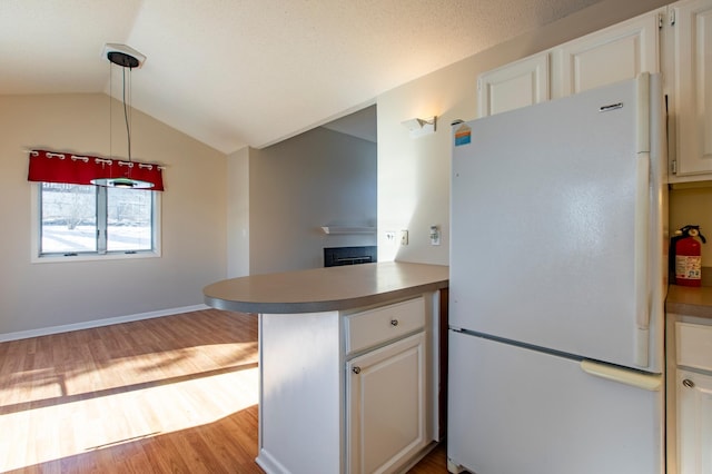 kitchen featuring freestanding refrigerator, wood finished floors, a peninsula, vaulted ceiling, and white cabinetry