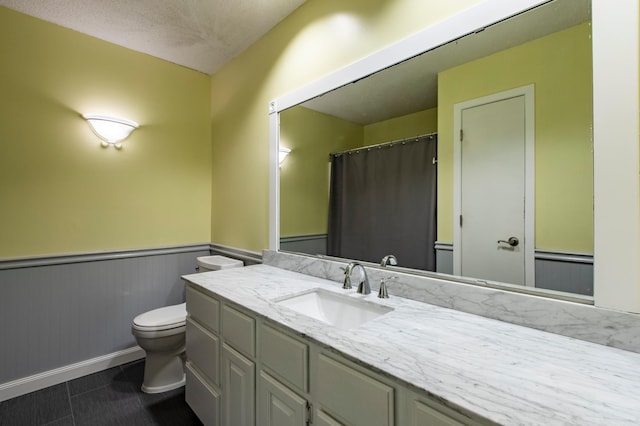 full bathroom with a wainscoted wall, toilet, vanity, tile patterned floors, and baseboards
