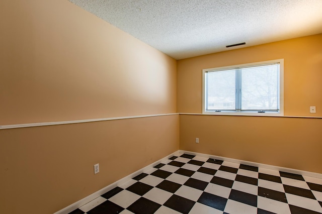 empty room with tile patterned floors, a textured ceiling, and baseboards