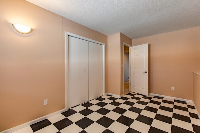 unfurnished bedroom with light flooring, a textured ceiling, a closet, and baseboards
