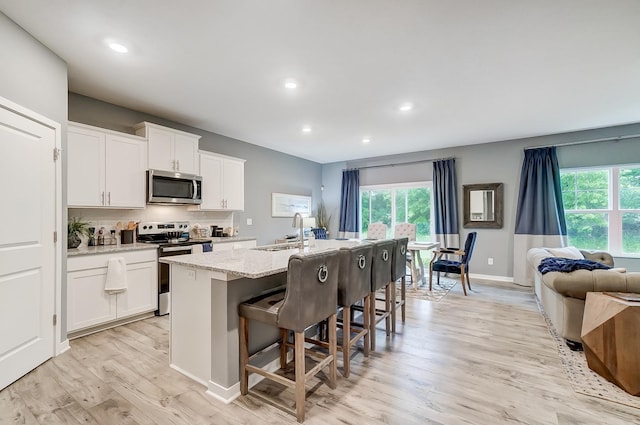 kitchen with a sink, a breakfast bar, light wood-type flooring, stainless steel appliances, and a kitchen island with sink