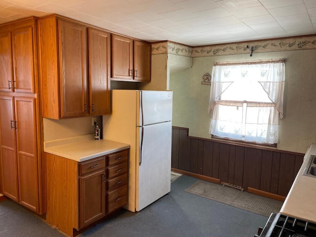 kitchen with white refrigerator, dark colored carpet, and wood walls