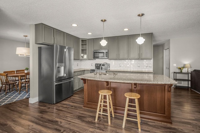 kitchen with appliances with stainless steel finishes, a kitchen island with sink, light stone countertops, and decorative light fixtures