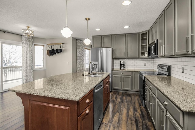 kitchen featuring dark wood-type flooring, stainless steel appliances, hanging light fixtures, and an island with sink