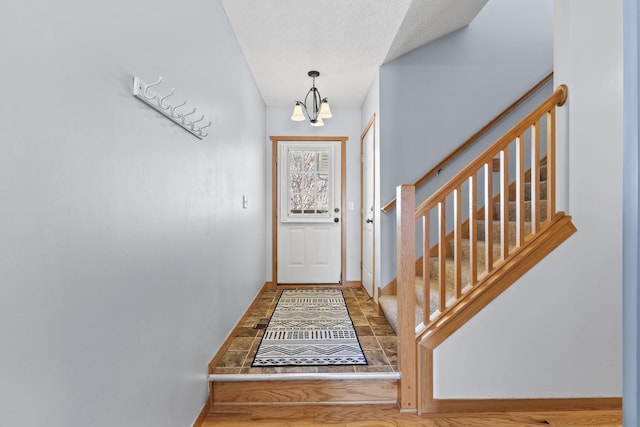 doorway to outside featuring a textured ceiling, stairs, baseboards, and a notable chandelier