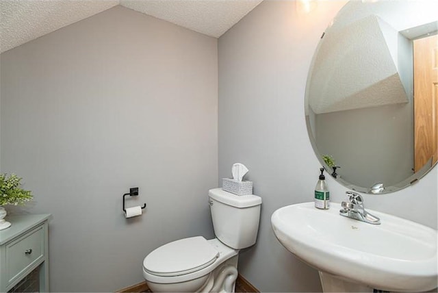 bathroom with sink, toilet, vaulted ceiling, and a textured ceiling