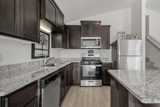 kitchen featuring stainless steel appliances, a sink, light wood-style floors, vaulted ceiling, and light stone countertops