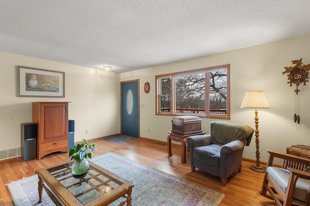 living area with a textured ceiling, light wood-type flooring, and visible vents