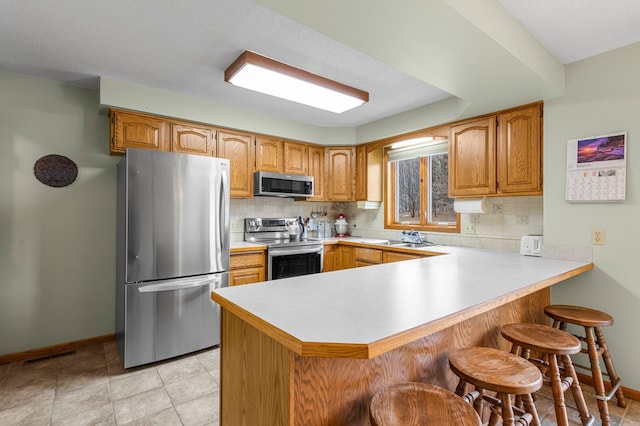 kitchen featuring a peninsula, light countertops, appliances with stainless steel finishes, backsplash, and a kitchen bar