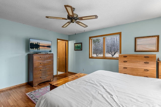 bedroom with a ceiling fan, wood-type flooring, a textured ceiling, and baseboards