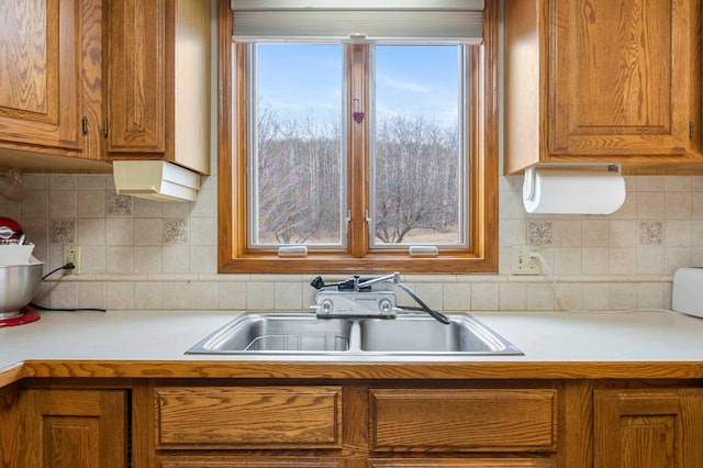 kitchen featuring backsplash, brown cabinets, a sink, and light countertops