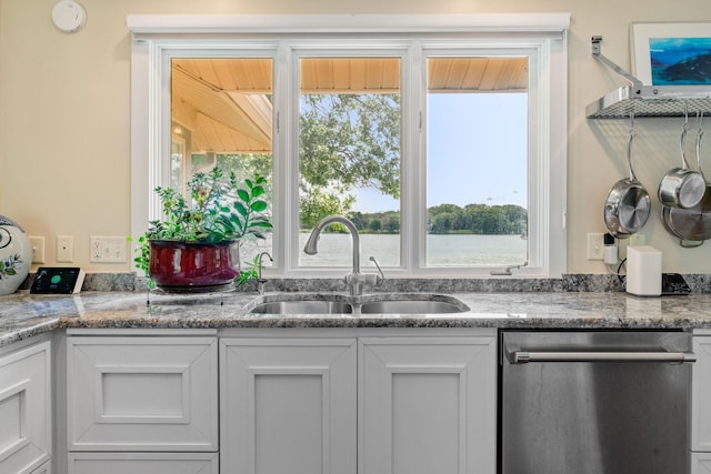 kitchen featuring white cabinets, a sink, stainless steel dishwasher, and light stone countertops