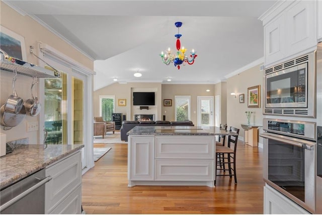 kitchen with a lit fireplace, appliances with stainless steel finishes, a kitchen bar, and light wood-style floors