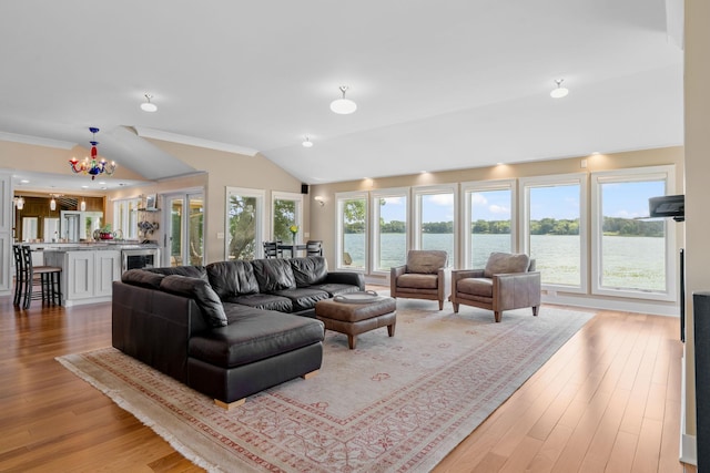 living room with light wood finished floors, a water view, an inviting chandelier, vaulted ceiling, and crown molding