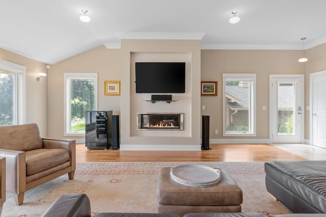 living area with crown molding, lofted ceiling, a glass covered fireplace, light wood-type flooring, and baseboards