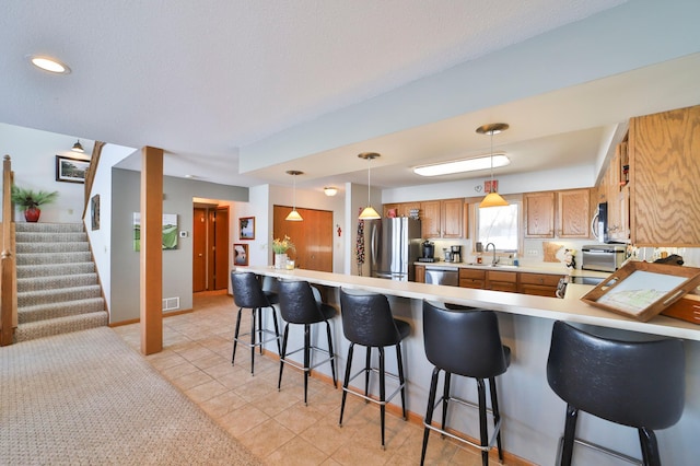 kitchen with brown cabinetry, a peninsula, stainless steel appliances, light countertops, and a sink